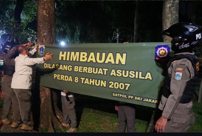 Petugas Satpol PP memasang spanduk larangan berbuat asusila di Taman Langsat, Kebayoran Baru, Jakarta Selatan, pada Jumat (13/6/2025) malam.