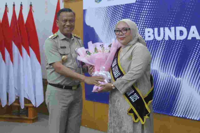 Momen Munjirin melempar senyum saat menyerahkan buket bunga kepada Essie Feransie Munjirin, yang dikukuhkan sebagai Bunda Literasi 2025, Senin (14/7/2025).