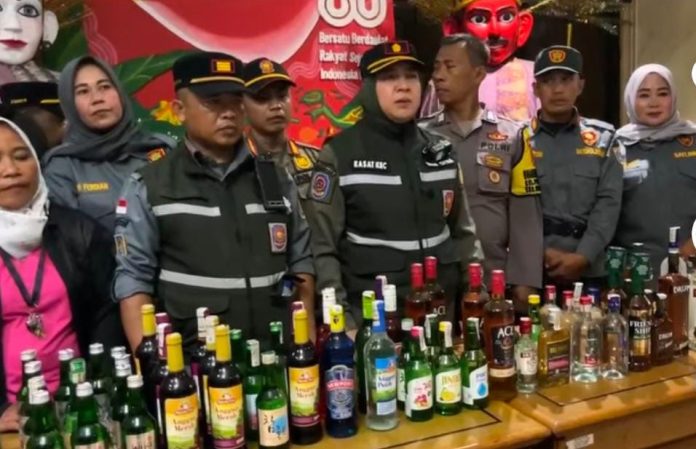 Kasatpol PP Kecamatan Kebayoran Lama, Dian Citra (tengah) memamerkan ratusan botol miras ilegal hasil penertiban dari sejumlah lokasi dengan kedok warung kelontong dan pedagang jamu, Rabu (11/3/2026).